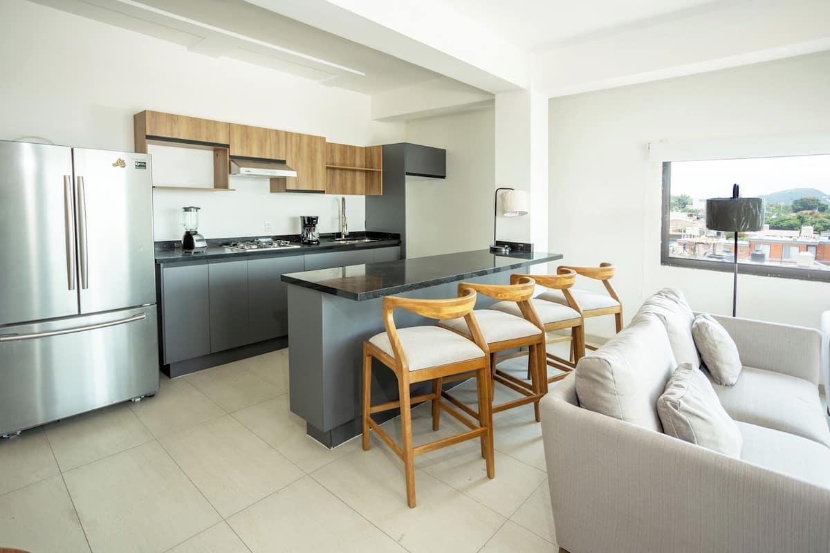 Una cocina moderna con una isla central, sillas de madera, un sofá y vistas por una ventana.