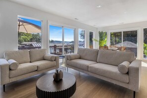 En moderne stue med to sofaer, et sofabord og store vinduer med udsigt til det fri.