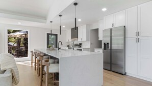 A modern kitchen with white cabinetry, a central island with bar stools, stainless steel appliances, and pendant lighting.