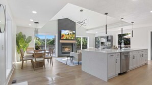 A modern kitchen with a central island, a dining area with a table and chairs, and a fireplace.