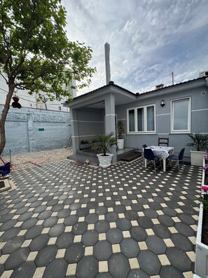 Ein Haus mit einer gefliesten Terrasse, einem überdachten Sitzbereich und einem kleinen Tisch mit Stühlen.