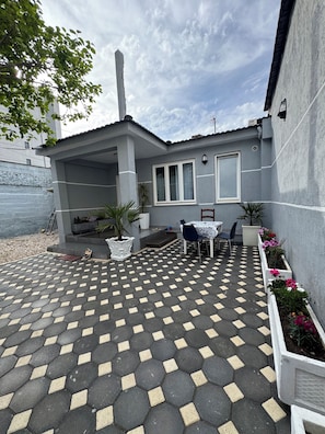 En overdækket terrasse med et mønstret flisegulv, siddepladser og en potteplante.