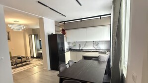 Una cucina moderna con mobili bianchi, un frigorifero nero e una zona pranzo con un tavolo in legno scuro e sedie grigie.