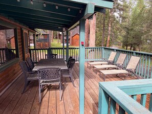 Una terraza techada al aire libre con una mesa y sillas, rodeada de barandillas de madera y árboles.