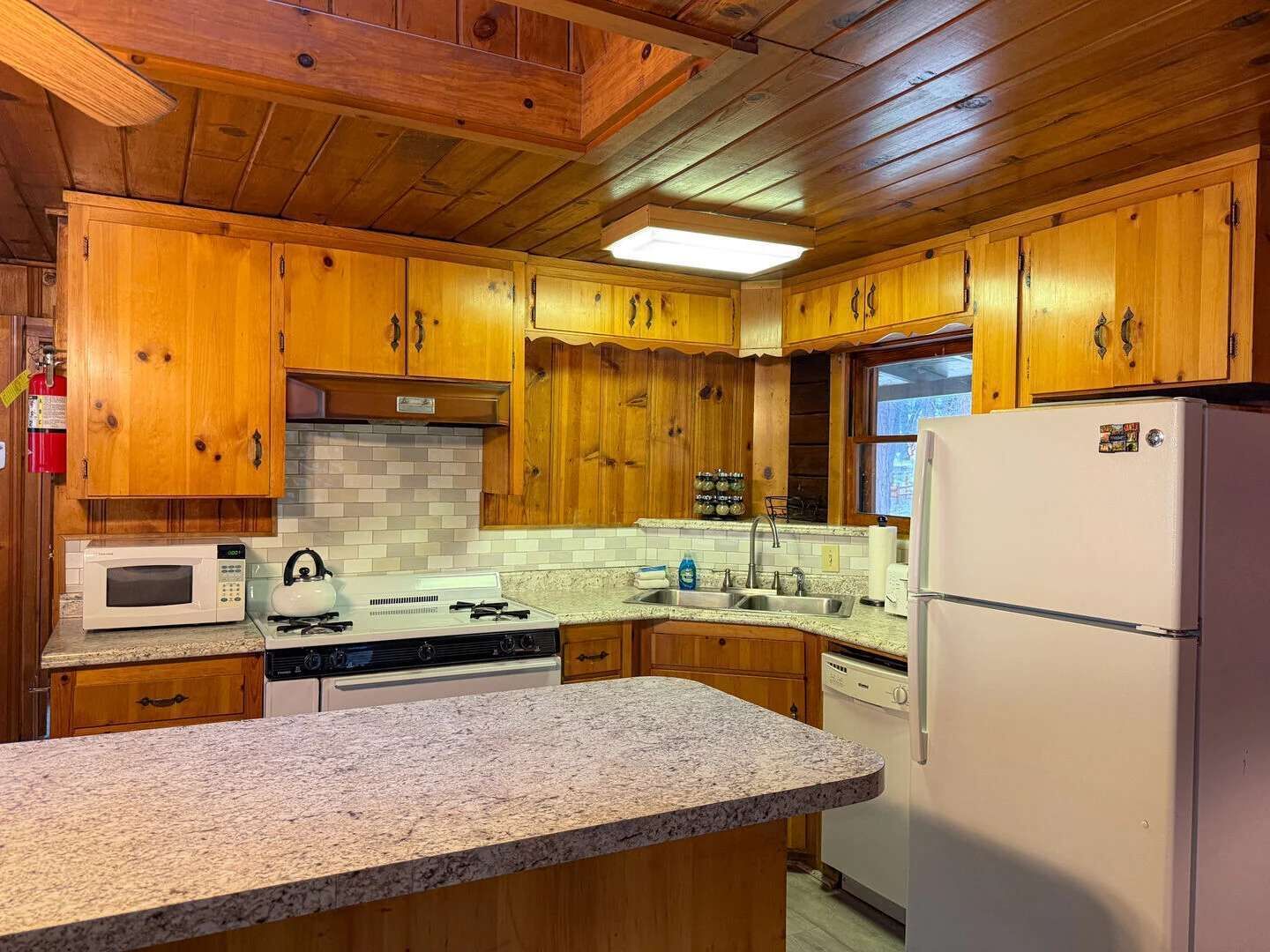 A kitchen with wooden cabinets, a microwave, stove, sink, and a refrigerator.