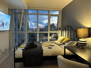 A bedroom with a large window, a bed, a desk, and a chair. - FIFA unobstructive view CN TOWER lakeshore 1+1(den) 2b1b condo with parking (Toronto)