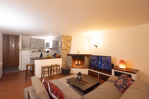 A living room with a fireplace, a sofa, a coffee table, and a kitchen area in the background.