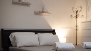 Un letto rifatto con lenzuola bianche, una lampada da comodino e una piccola pianta in vaso su uno scaffale sopra il letto.
