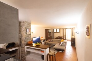A living room with a stone wall, a television, a sofa, a dining area, and a kitchen.