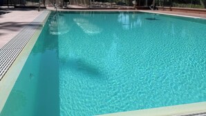 Una piscina con acqua cristallina, circondata da alberi e ombreggiata da ombrelloni.