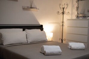 Ein ordentlich bezogenes Bett mit weißen Leinen, eine Nachttischlampe und ein dekorativer Metallständer.