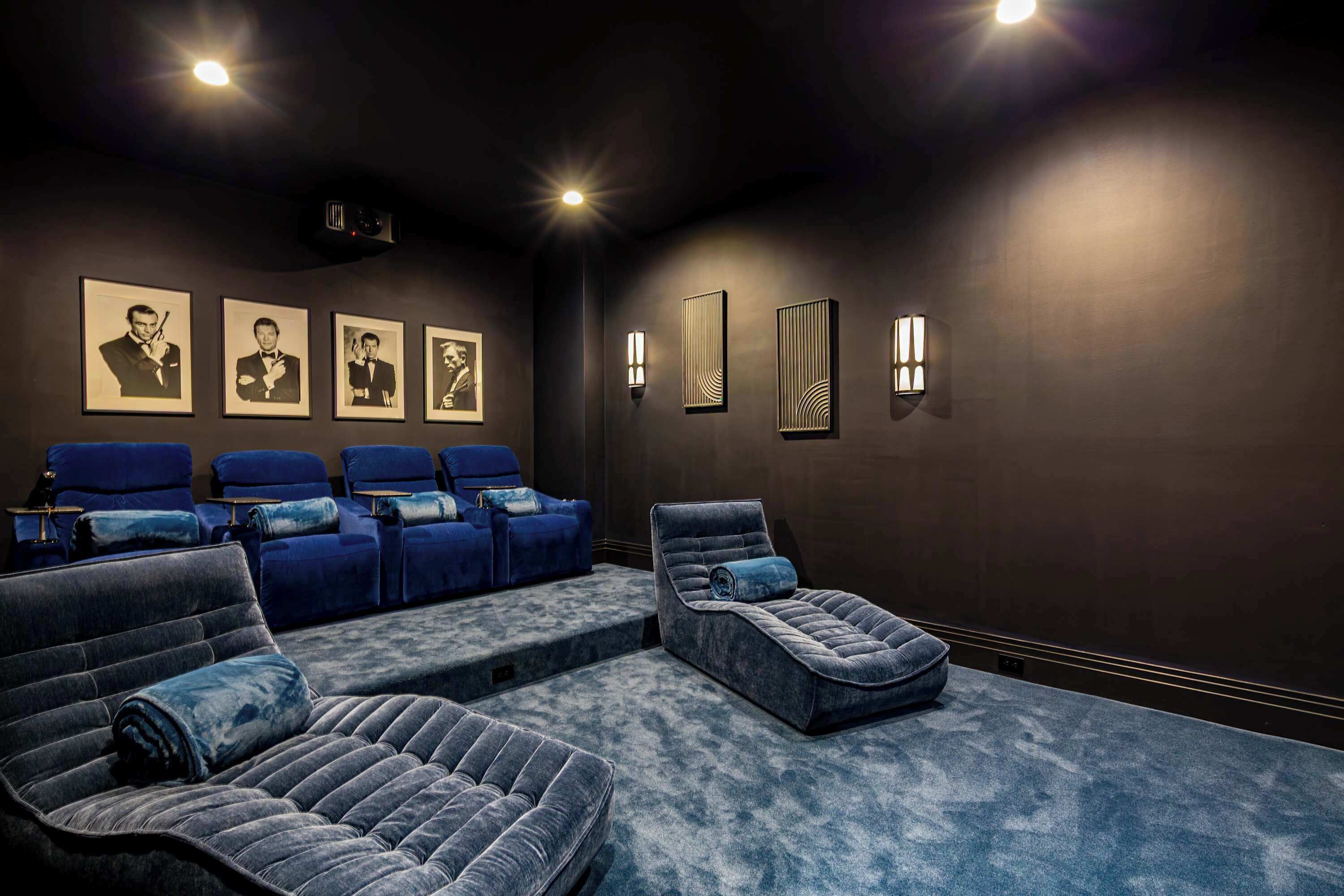 A dark-themed cinema room with reclining chairs, a large screen, and framed pictures on the wall.