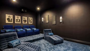 A dark-themed cinema room with reclining chairs, a large screen, and framed pictures on the wall.
