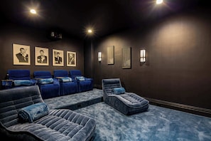 Una sala de cine con ambiente oscuro, sillones reclinables, una pantalla grande y cuadros en la pared.