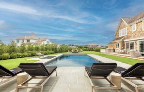A swimming pool with lounge chairs, a patio area, and a view of surrounding houses.