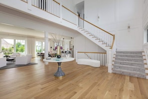 A spacious living area with a high ceiling, a staircase, and a dining area.