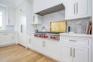 Uma cozinha com armários brancos, fogão de aço inoxidável e painel de mármore.
