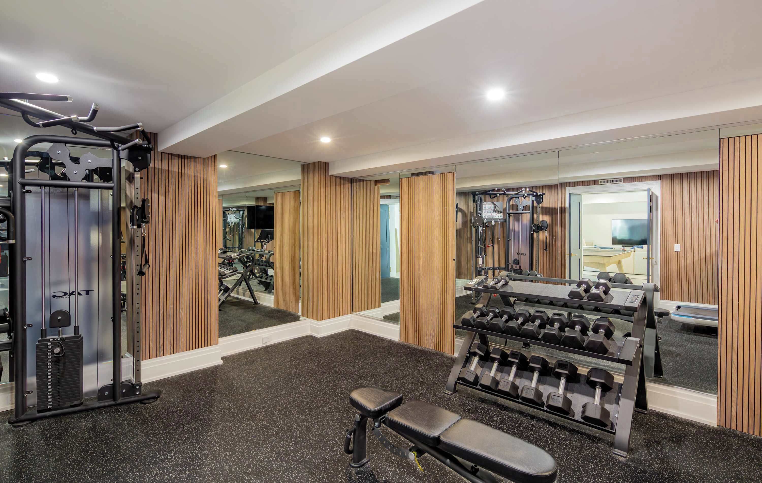 A gym with exercise equipment, mirrors, and wooden paneling.
