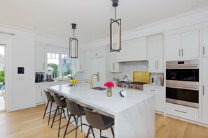 A modern kitchen with white cabinetry, a marble island, bar stools, stainless steel appliances, and pendant lighting.
