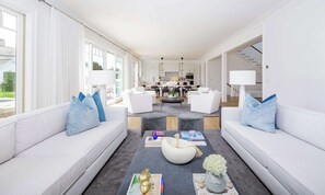 A modern living room with white sofas, a coffee table, and a view of the kitchen.