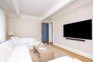A modern living room with a white sofa, a coffee table, a TV mounted on the wall, and a blue door. - Rosko Estate by Rove Travel Villa With Pool &court (Southampton)
