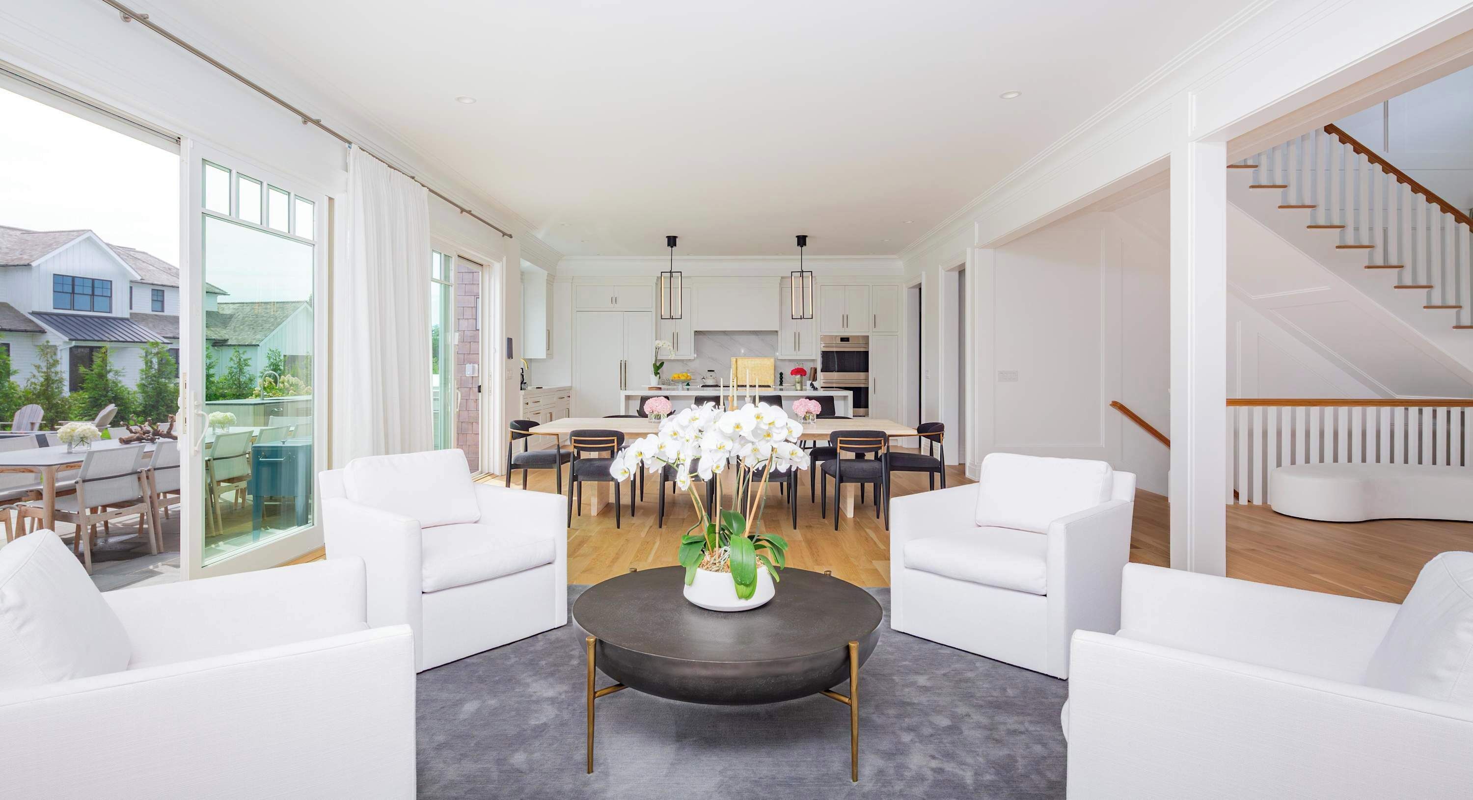 A modern living room with white furniture, a dining area, and a staircase.