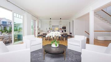 A modern living room with white furniture, a dining area, and a staircase.