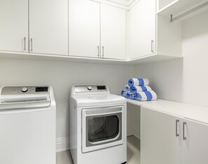 A laundry area with a front-loading washer and dryer, a stack of towels, and white cabinets.