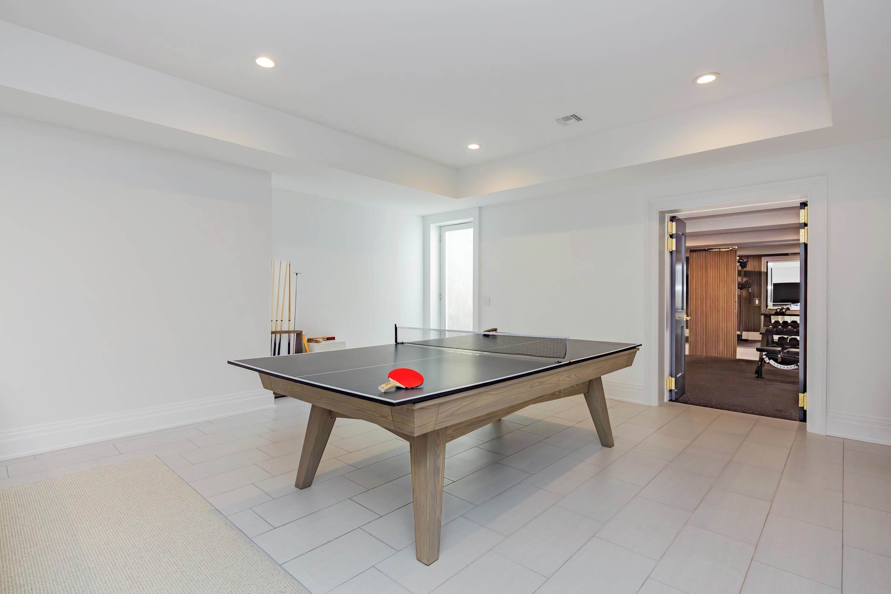 Una mesa de ping pong en una habitación con paredes blancas y una puerta que da a otra estancia.