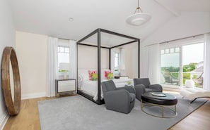 A modern bedroom with a four-poster bed, a grey sofa, a round coffee table, and a large window offering a view. - Rosko Estate by Rove Travel Villa With Pool &court (Southampton)