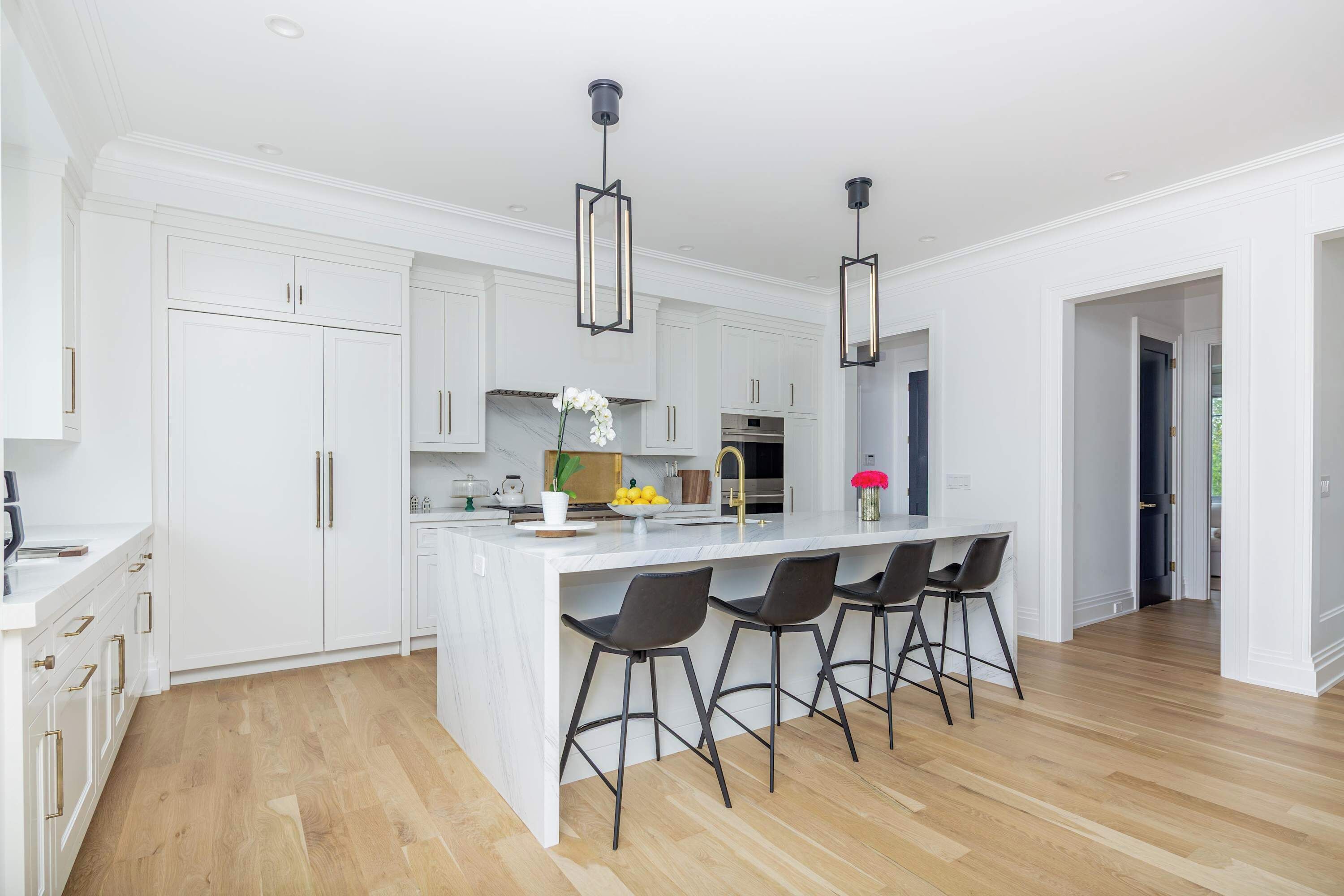 Cozinha moderna com armários brancos, uma ilha central com banquetas e iluminação pendente.
