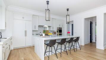 Cozinha moderna com armários brancos, uma ilha central com banquetas e iluminação pendente.