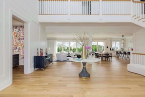 A spacious living area with a central round table, a dining area with chairs, and a staircase leading to an upper level.