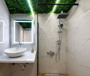 A bathroom with a white sink, a mirror, a shower with a handheld showerhead, and a green artificial ceiling.