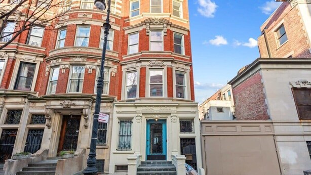 A corner building with a bay window, a blue door, and a fire escape.
