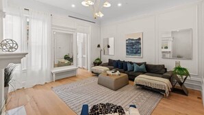 A spacious living room with a sofa, ottoman, and a large window with sheer curtains.