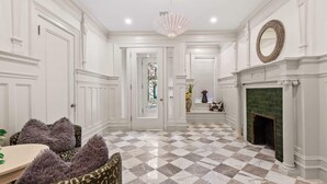 A spacious room with a checkered floor, white walls, a fireplace, and a chandelier.