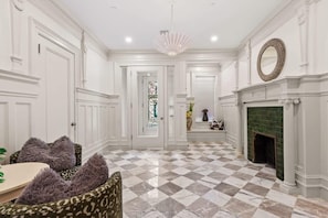 A spacious room with a checkered floor, white walls, a fireplace, and a chandelier.