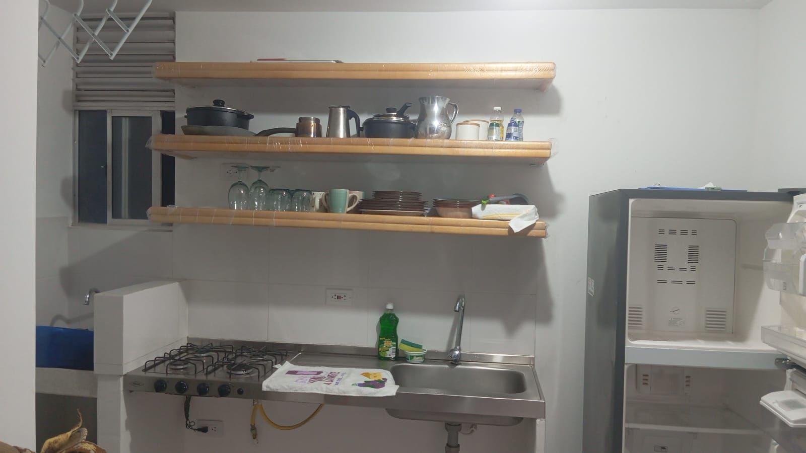A compact kitchen with a gas stove, a sink, and wooden shelves above containing kitchenware.