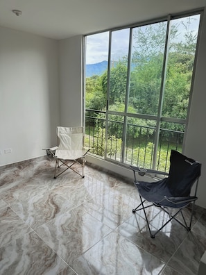 Quarto com uma janela grande, uma cadeira dobrável e uma cadeira.