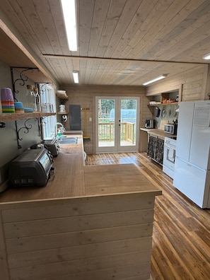 Interior de madera con área de cocina, que incluye un refrigerador, microondas y una cafetera.