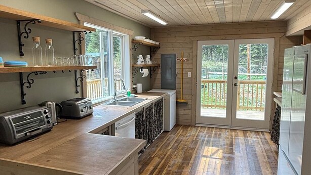 A kitchen with wooden floors, a countertop with appliances, and a view to the outside. - Private Cariboo Retreat -House & Cabin Lakes, Fishing, Hunting ,Trails, Outdoor (Forest Grove)