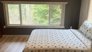 A bedroom with a large window, wooden flooring, and a bed with patterned bedding. - Private Cariboo Retreat -House & Cabin Lakes, Fishing, Hunting ,Trails, Outdoor (Forest Grove)