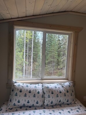 Ein Zimmer mit großem Fenster, einem Bett mit gemusterten Betttextilien und Blick auf einen Wald.
