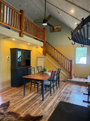 A dining area with a wooden table, chairs, a ceiling fan, and a staircase.