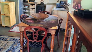 A dining area with a wooden table and chairs, a woven basket, and a kitchen in the background.