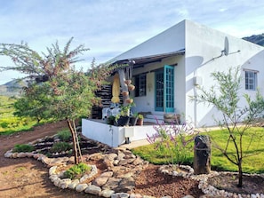 Une maison moderne à l’extérieur blanc, dotée d’un porche abrité et d’un jardin agrémenté de rochers et de plantes.