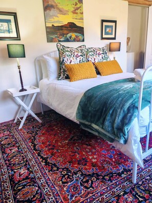 Un lit avec un cadre blanc, une couverture à motifs et un tapis coloré.