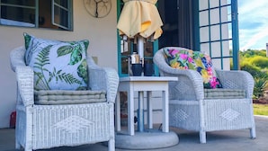 Deux fauteuils en osier avec des coussins, une petite table et un parasol jaune.
