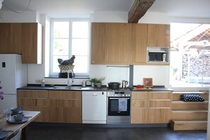 A modern kitchen with wooden cabinets, a dishwasher, an oven, a microwave, and a window with a view of the outdoors. - Renovated house in an old farmhouse 12km from the center of Brussels (Sint-Pieters-Leeuw)